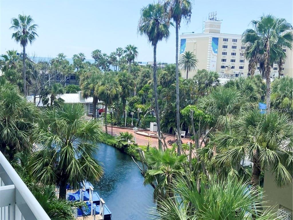 An elevated view of a tropical courtyard with a canal, palm trees, and a hotel building — 5500 GULF BOULEVARD UNIT 4256, ST PETERSBURG, FL