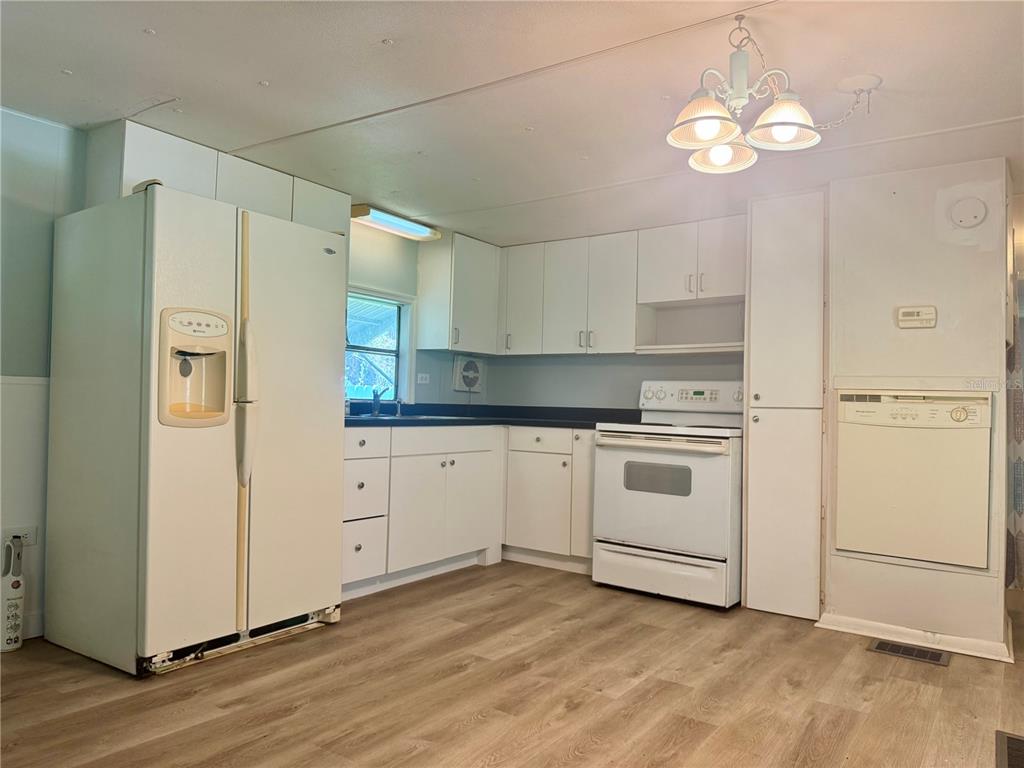 A kitchen features white cabinets, white appliances, a dark countertop, and light wood-look flooring — 3405 FREMONT LANE, SPRING HILL, FL
