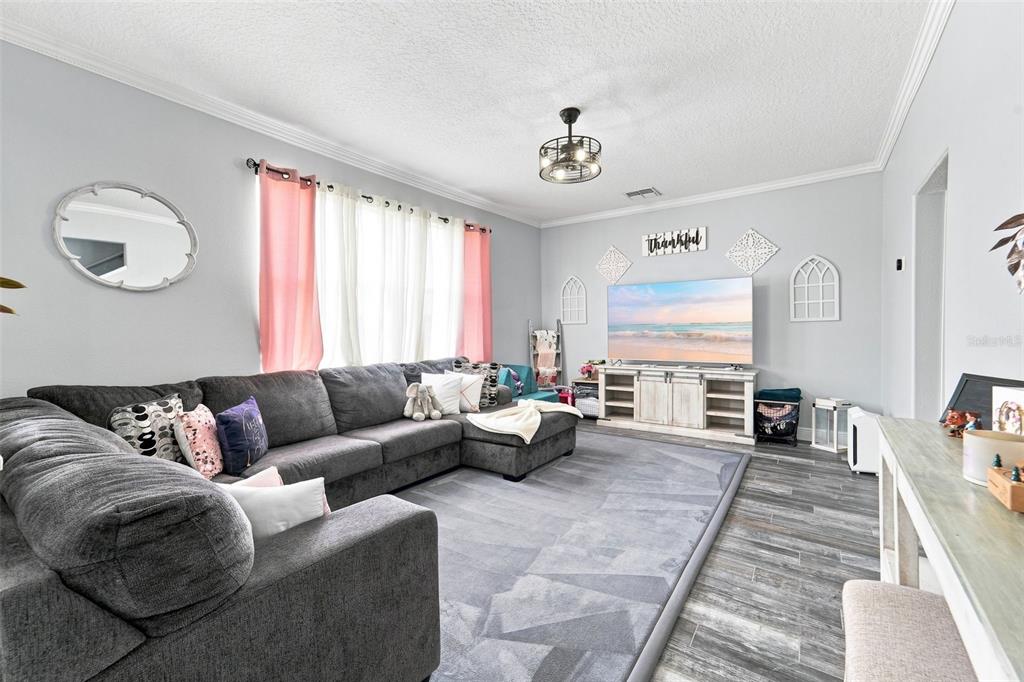 A living room features a large gray sectional sofa, a television, and wood-look tile flooring — 9773 BENNINGTON CHASE DRIVE, ORLANDO, FL