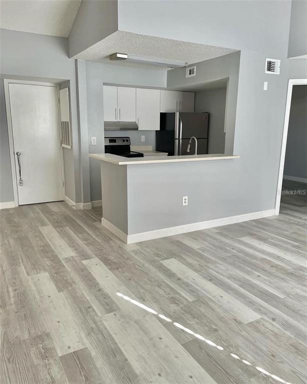 A kitchen with white cabinets and stainless steel appliances overlooks a living area with wood-look flooring — 425 FOUNTAINHEAD CIRCLE UNIT 208, KISSIMMEE, FL