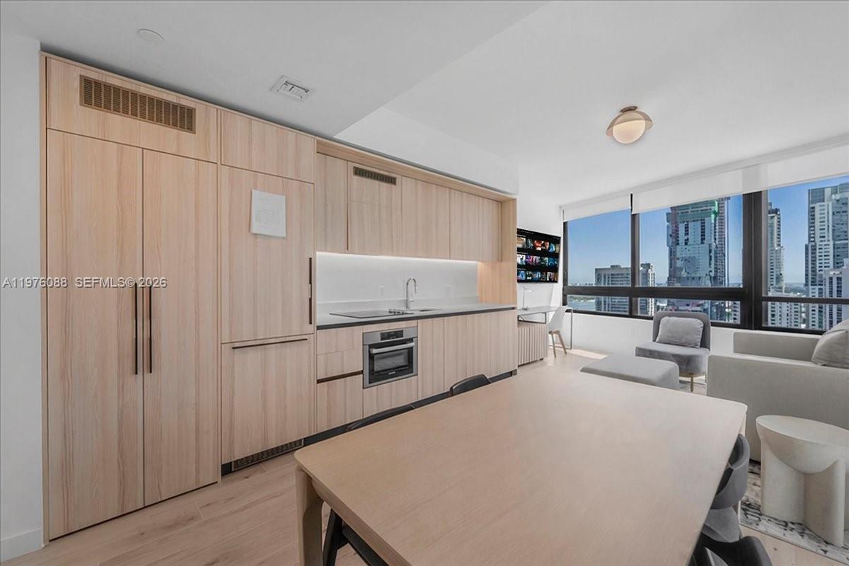 A modern kitchen with light wood cabinetry and integrated appliances overlooks a city skyline — 225 N Miami # 3009, Miami FL 33128, MIAMI, FL