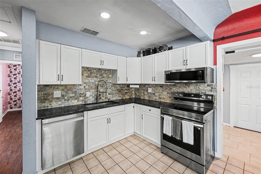A kitchen features white cabinets, stainless steel appliances, dark countertops, and a stone tile backsplash — 3719 39TH STREET N, ST PETERSBURG, FL