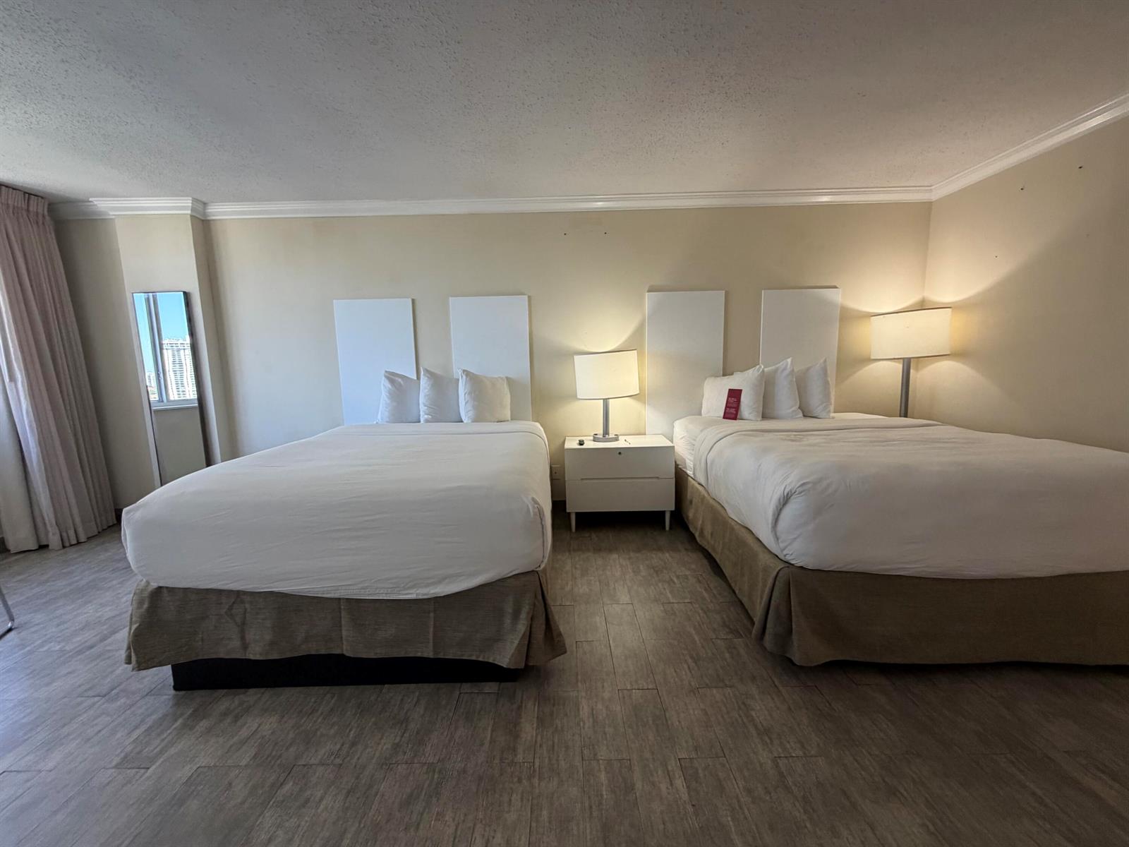 A hotel room features two beds with white linens, a central nightstand, and wood-look flooring — 19201 Collins Avenue, Sunny Isles Beach FL 33160, SUNNY ISLES BEACH, FL