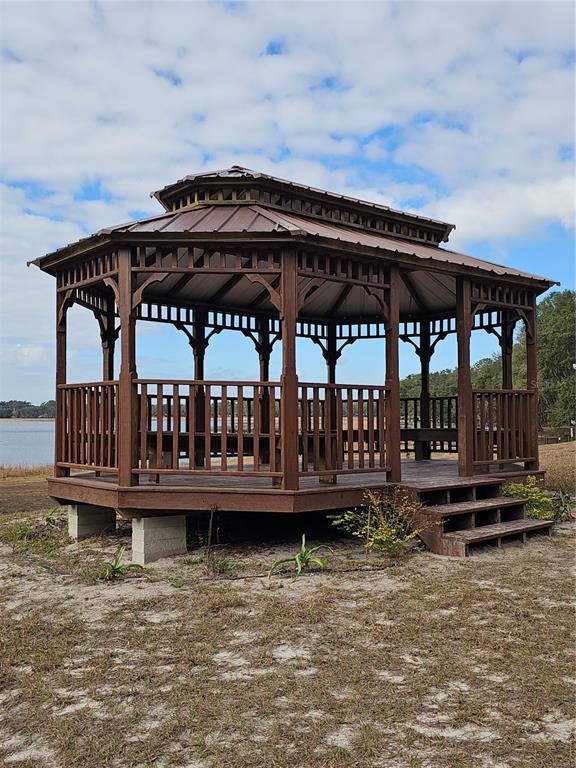 A wooden gazebo with a metal roof sits on a sandy lot near a lake — TBD SE 136TH TERRACE, DUNNELLON, FL