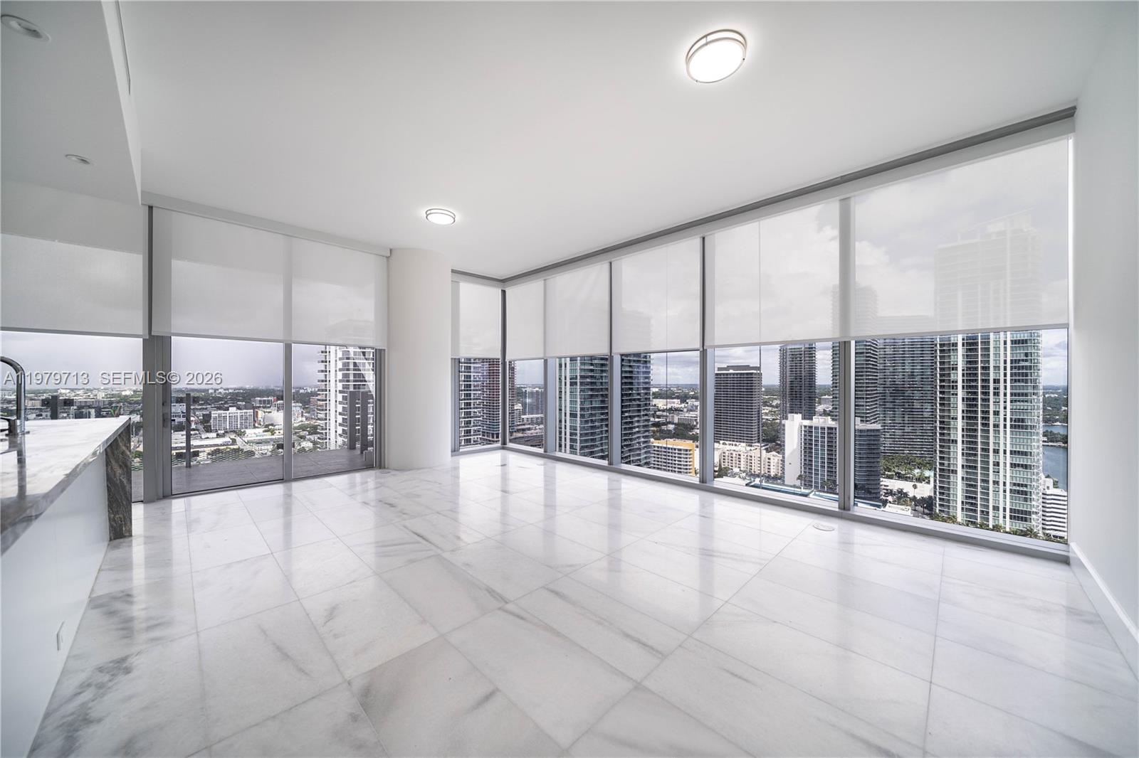 An empty room with white marble floors, floor-to-ceiling windows, and city skyline views — 700 NE 26TH TER # 3006, Miami FL 33137, MIAMI, FL