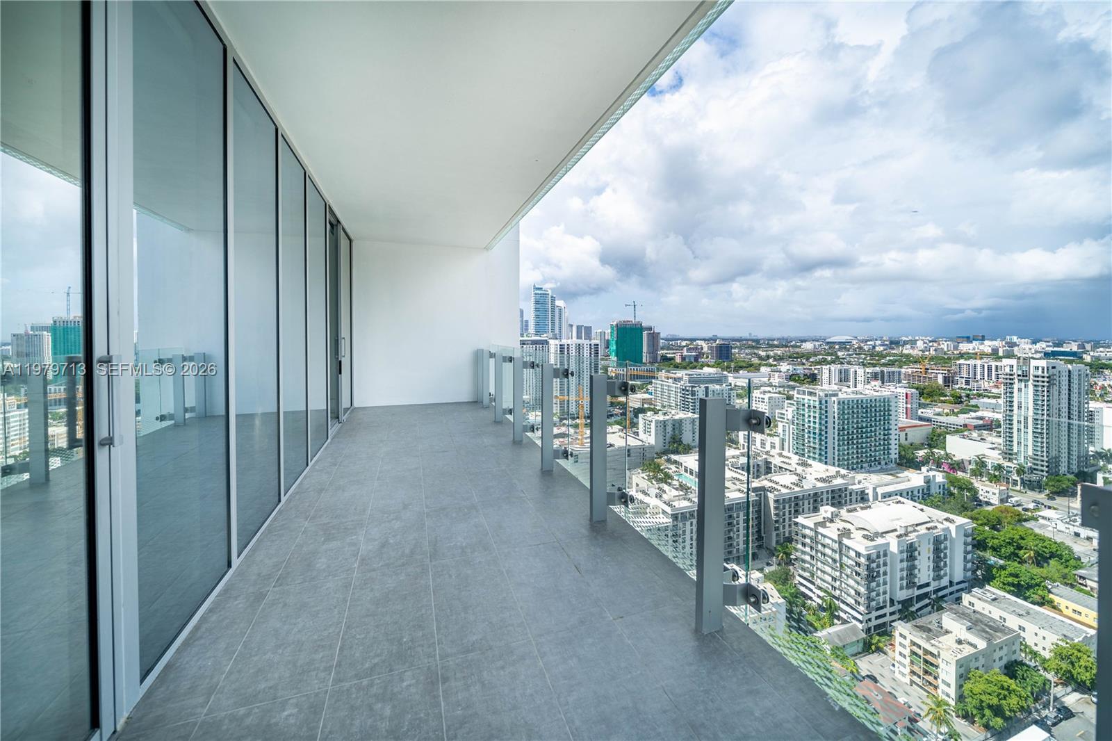 A high-rise balcony features gray tile flooring, a glass railing, and expansive city views — 700 NE 26TH TER # 3006, Miami FL 33137, MIAMI, FL