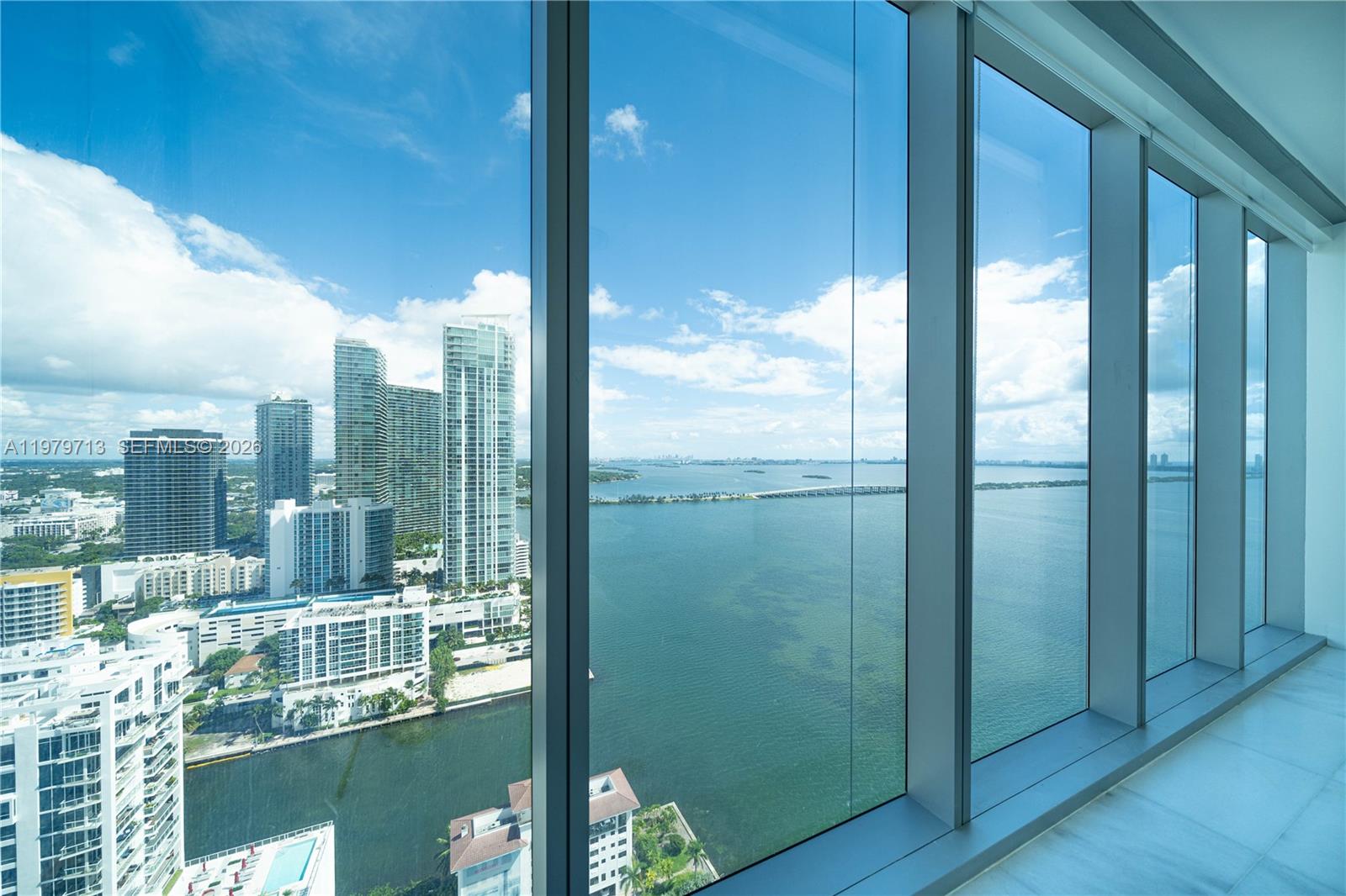 A high-rise room features floor-to-ceiling windows overlooking a bay, city skyline, and bridge — 700 NE 26TH TER # 3006, Miami FL 33137, MIAMI, FL