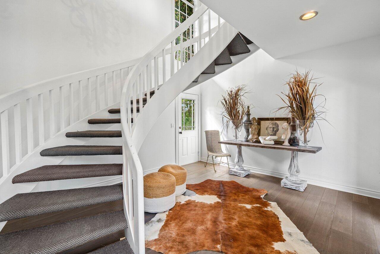 A curved staircase with a dark runner leads up from a foyer with a cowhide rug — 11823 Pebblewood Drive, Wellington FL 33414, WELLINGTON, FL