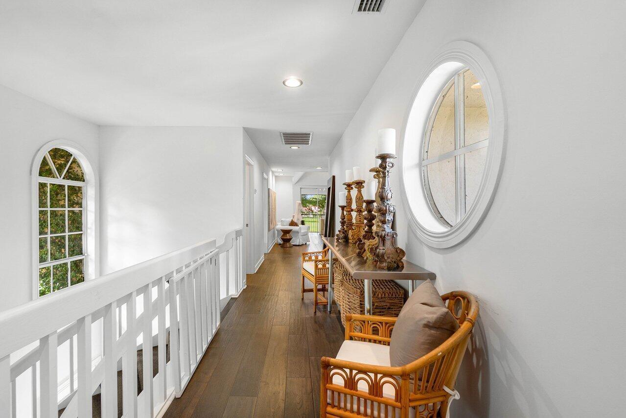A hallway with wood floors, a white railing, and a round window overlooking a room — 11823 Pebblewood Drive, Wellington FL 33414, WELLINGTON, FL