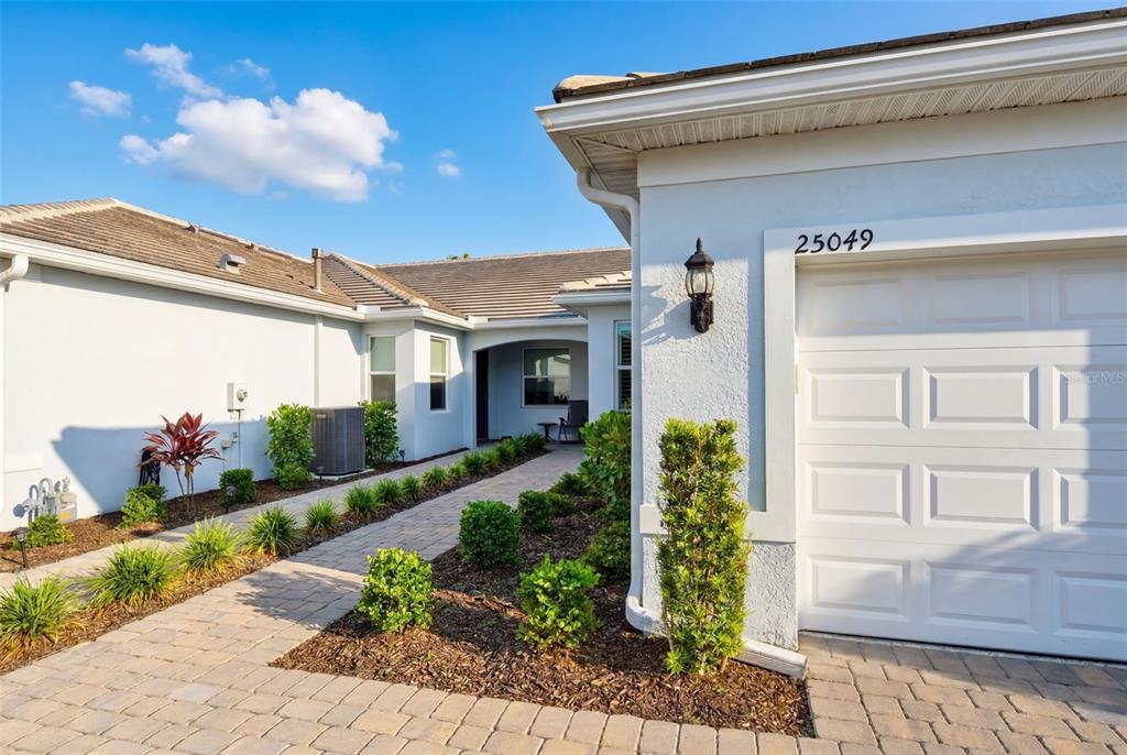 A paved walkway leads to the entrance of a house with a white garage door — 25049 PEARL LAKE CIRCLE, ENGLEWOOD, FL