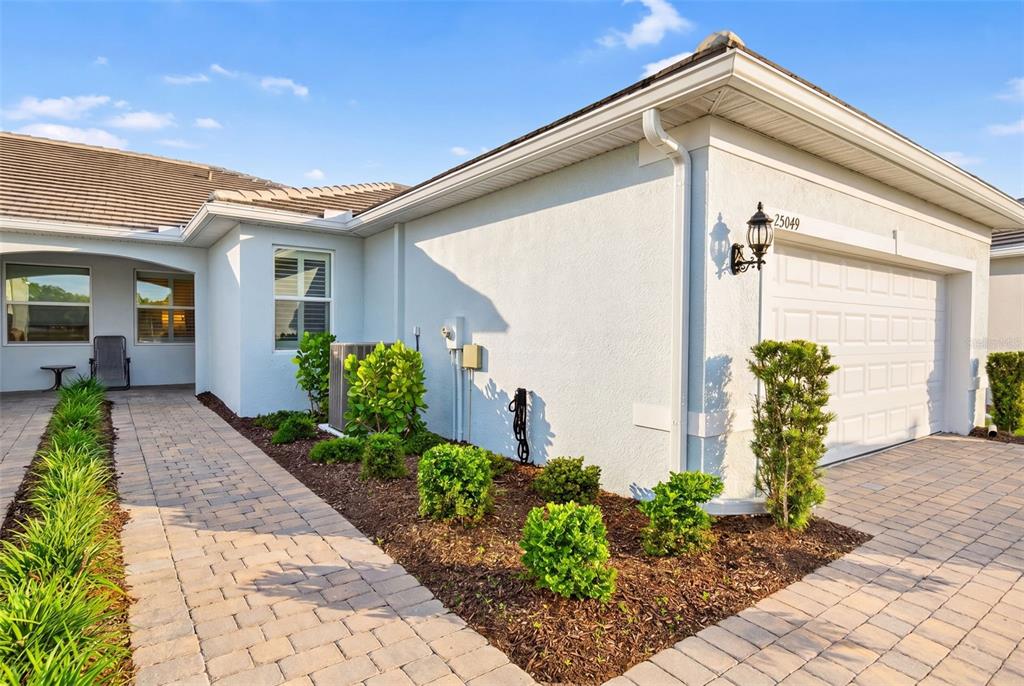 The exterior of a light-colored house features a paved walkway, a garage, and landscaping — 25049 PEARL LAKE CIRCLE, ENGLEWOOD, FL