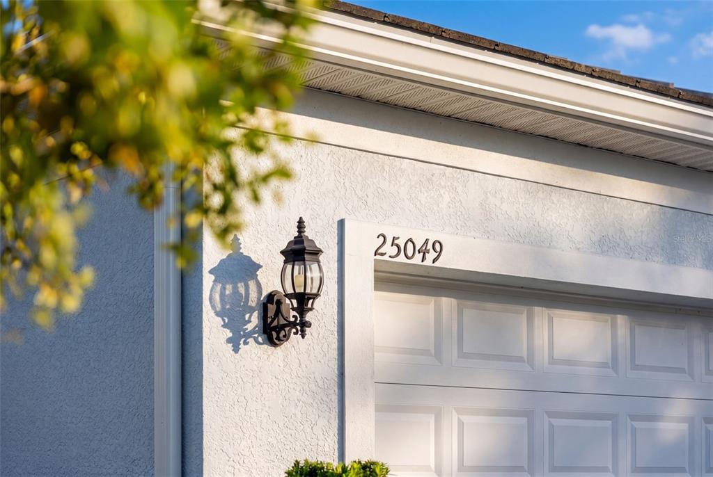 A close-up view of a white stucco exterior wall featuring a black wall-mounted lantern — 25049 PEARL LAKE CIRCLE, ENGLEWOOD, FL