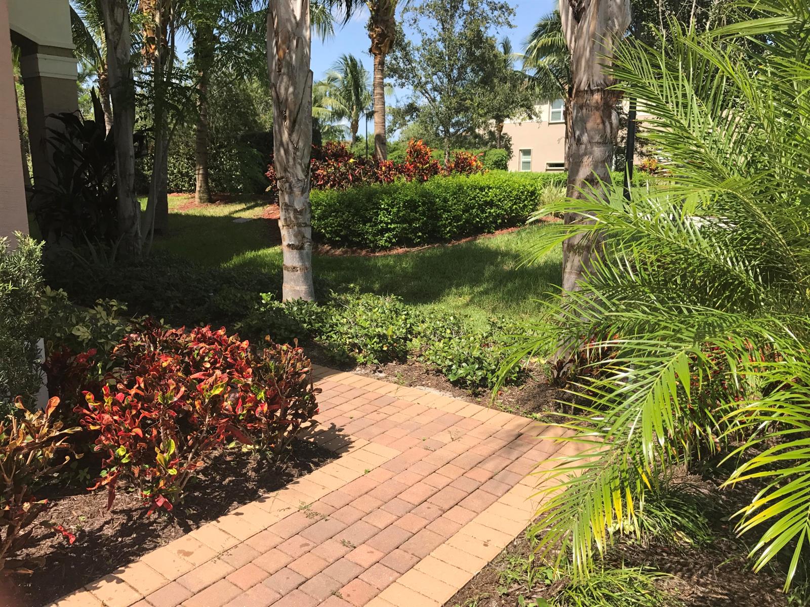 A brick walkway leads through a landscaped yard with palm trees and colorful shrubs — 8187 Half Dome Court, Boynton Beach FL 33473, BOYNTON BEACH, FL