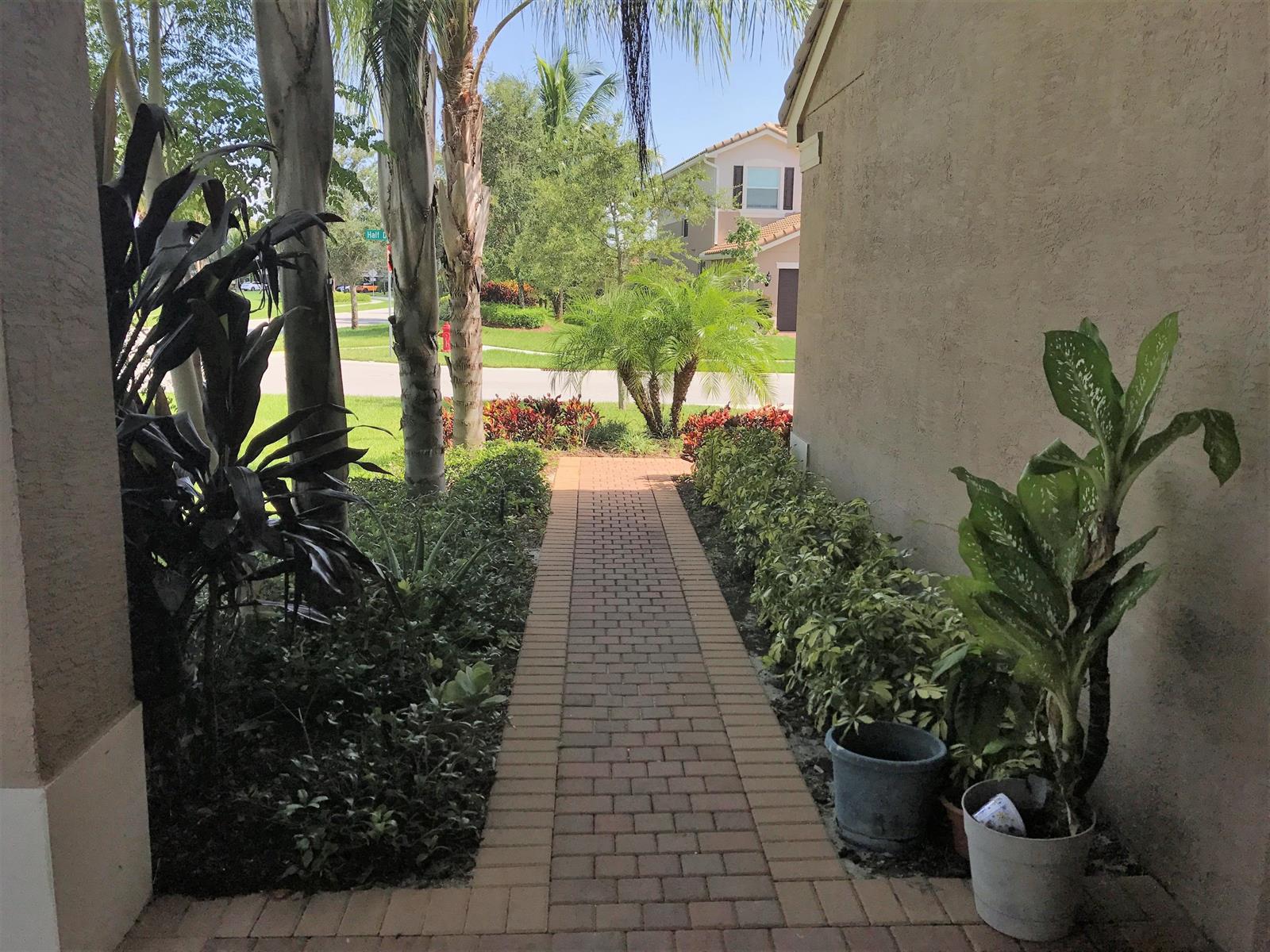 A brick walkway leads from a covered entryway toward a street and neighboring houses — 8187 Half Dome Court, Boynton Beach FL 33473, BOYNTON BEACH, FL