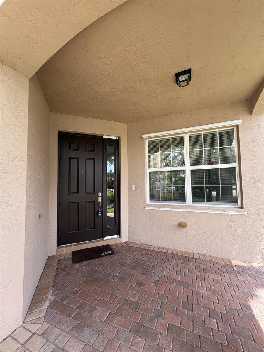 A covered entryway features a dark brown front door, a window, and brick pavers — 8187 Half Dome Court, Boynton Beach FL 33473, BOYNTON BEACH, FL