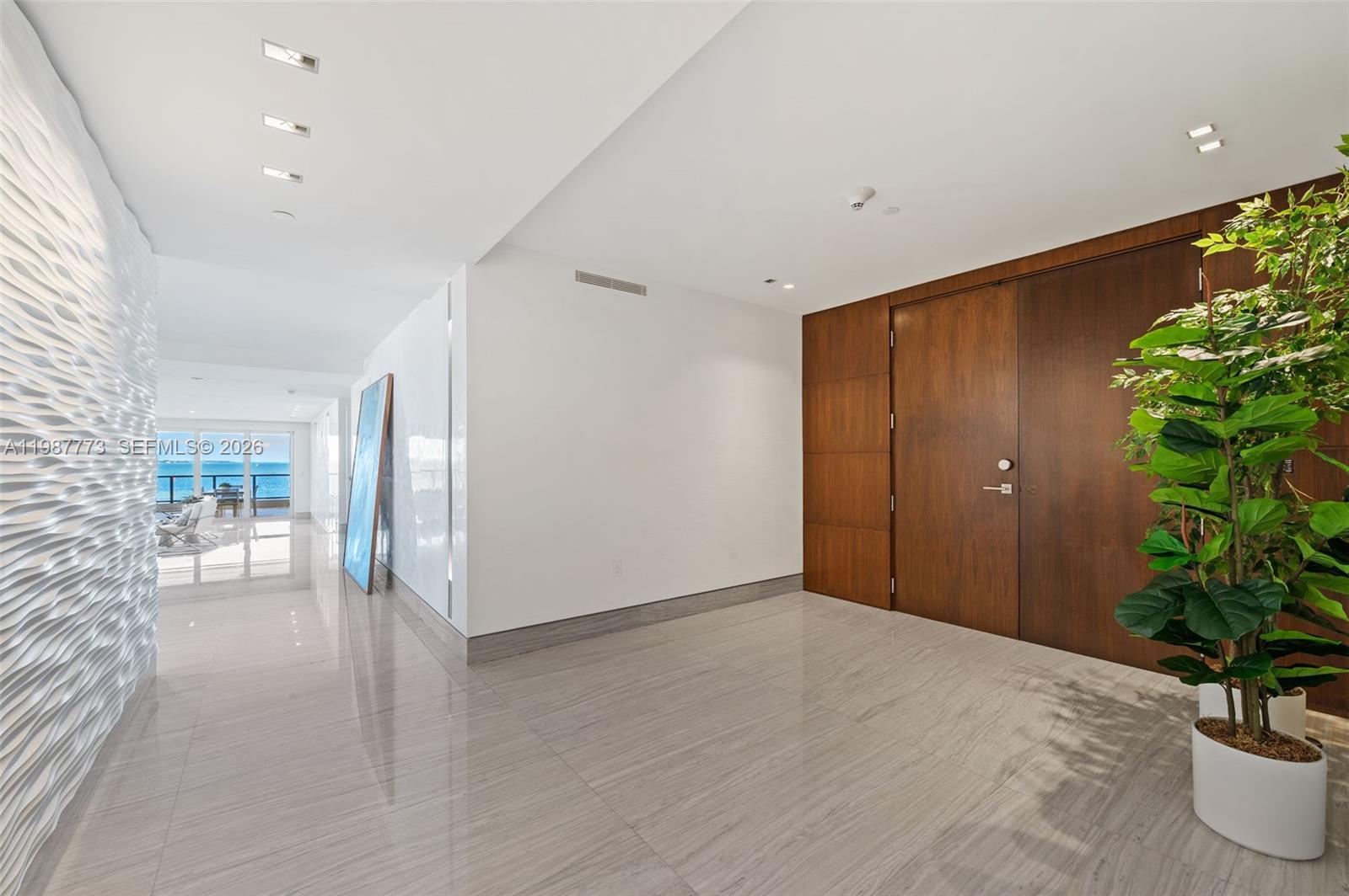 A modern entryway features a textured white wall, wood paneling, and polished tile flooring — 3535 Hiawatha Ave # 502, Miami FL 33133, MIAMI, FL