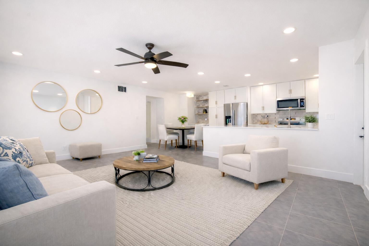 An open-concept living room and kitchen featuring white cabinetry, tile flooring, and neutral furniture — 203 Manatee Lane # A, Fort Pierce FL 34982, FORT PIERCE, FL