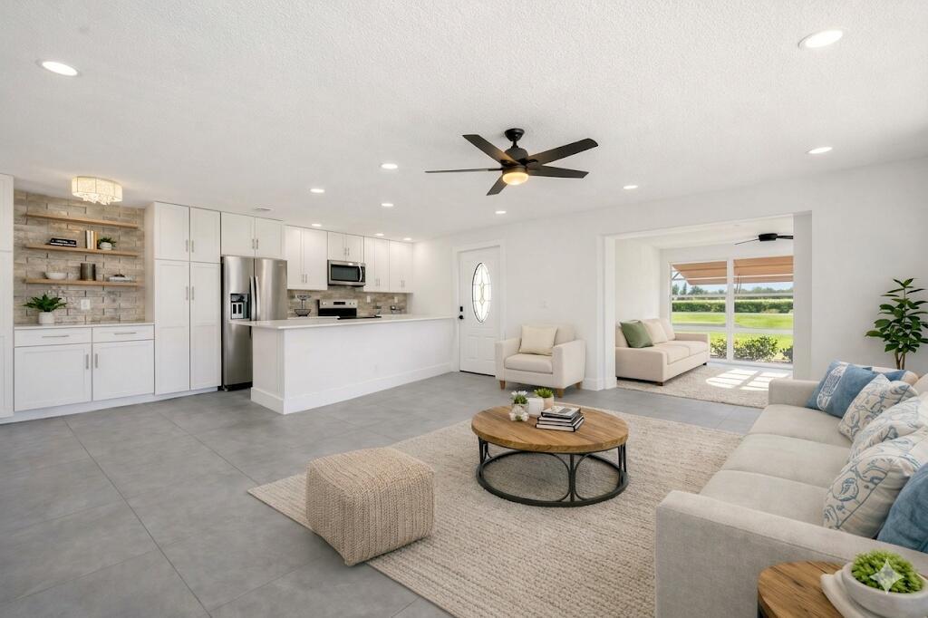 An open-concept living room and kitchen with white cabinetry, gray tile floors, and neutral furniture — 203 Manatee Lane # A, Fort Pierce FL 34982, FORT PIERCE, FL