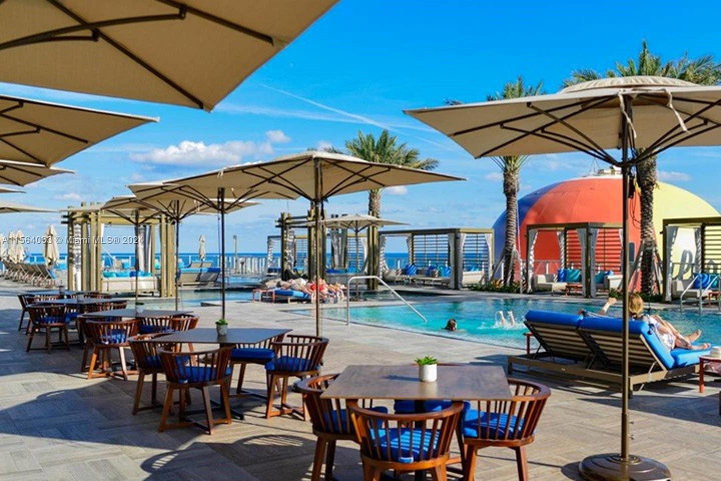 An outdoor pool deck features dining tables, lounge chairs, umbrellas, and a colorful dome structure — 4111 S Ocean Dr # 2101, Hollywood FL 33019, HOLLYWOOD, FL