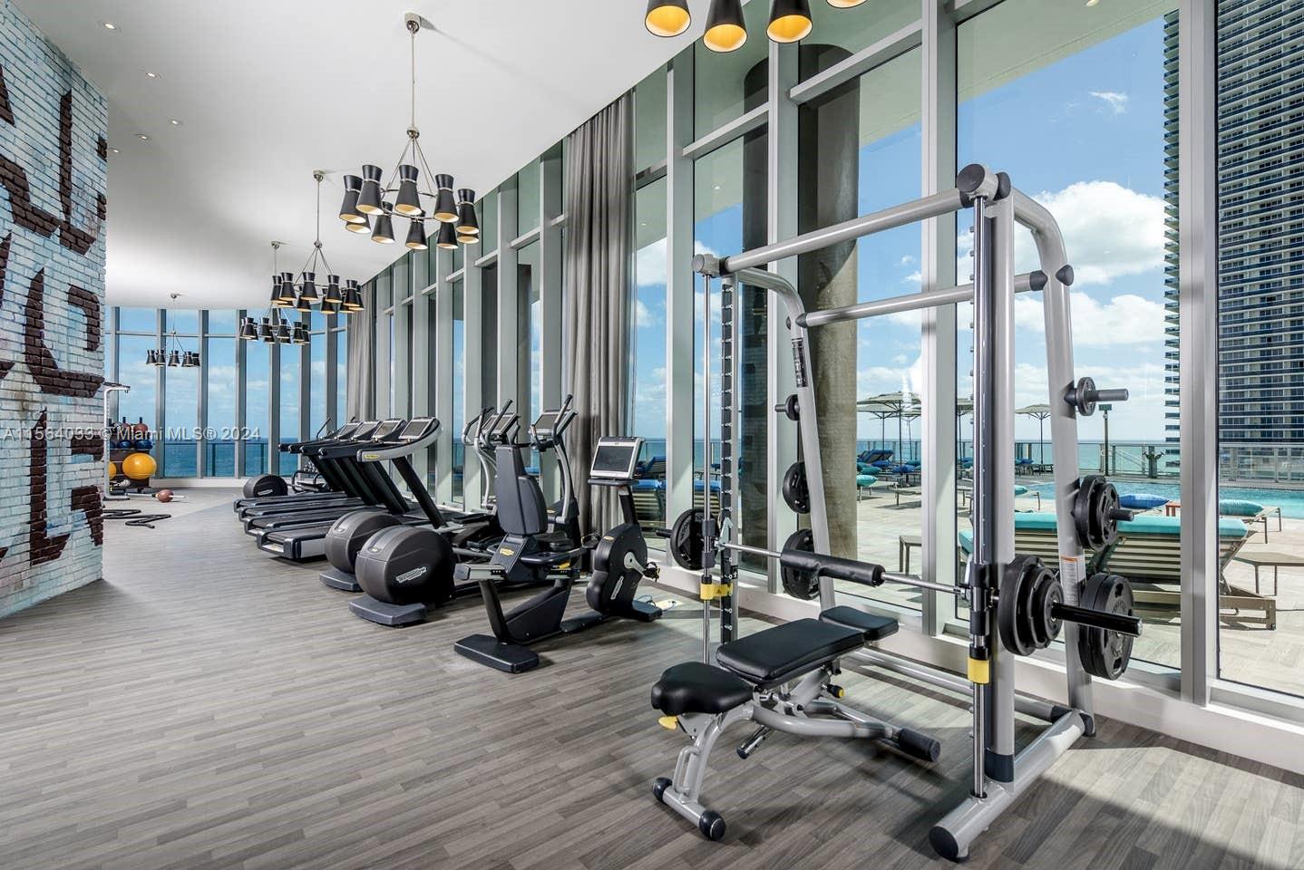 A modern fitness center features gym equipment, floor-to-ceiling windows, and views of an outdoor pool — 4111 S Ocean Dr # 2101, Hollywood FL 33019, HOLLYWOOD, FL