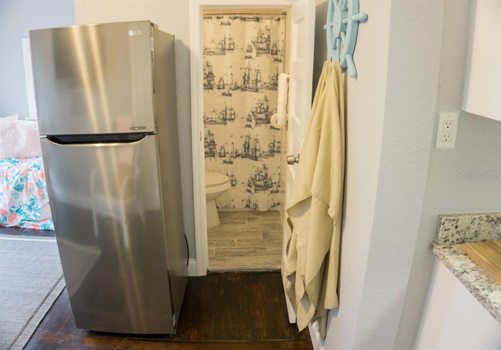 A stainless steel refrigerator stands next to a bathroom doorway featuring a nautical-themed shower curtain — 700 1ST STREET N UNIT 4, ST PETERSBURG, FL