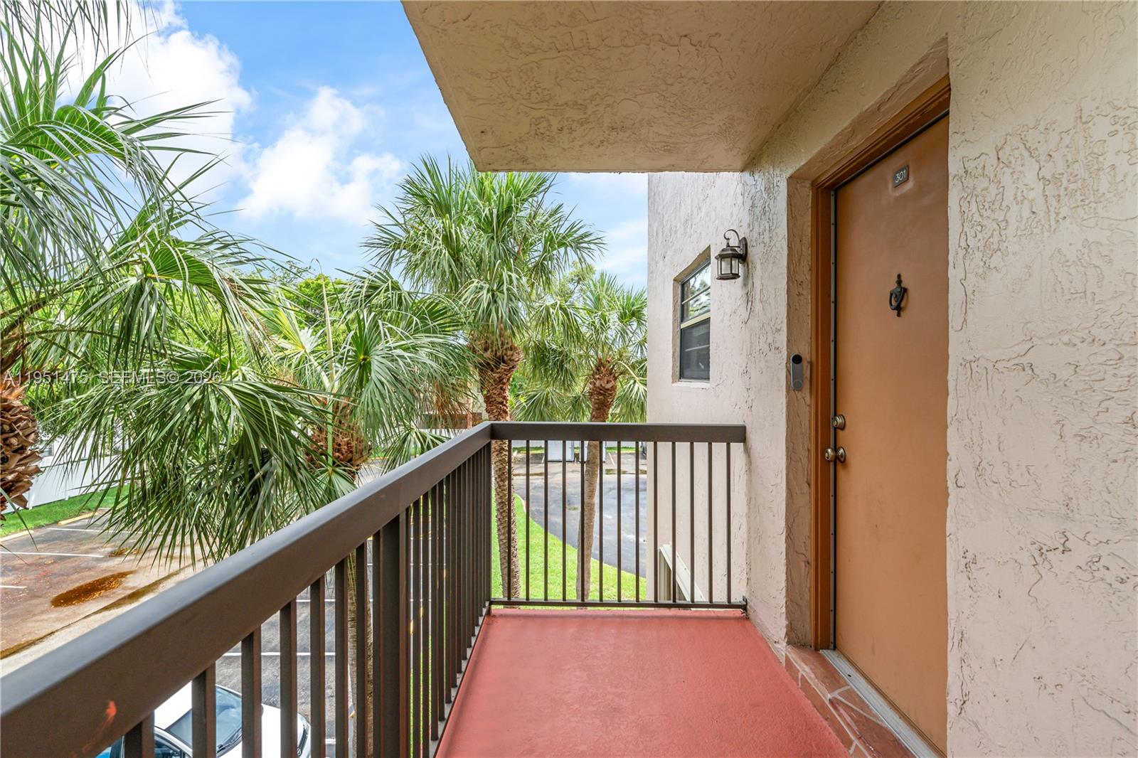 An outdoor balcony with a brown door, metal railing, and palm trees in the background — 4960 E Sabal Palm Blvd # 301, Tamarac FL 33319, TAMARAC, FL