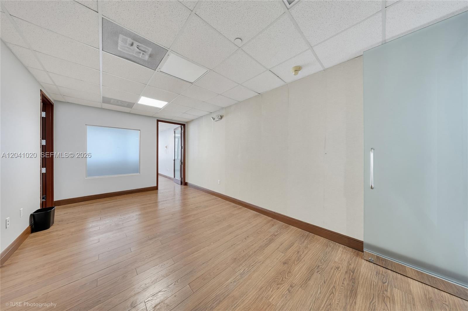 An empty office space features wood-look flooring, a drop ceiling, and a frosted glass door — 1200 Brickell Ave # D, Miami FL 33131, MIAMI, FL