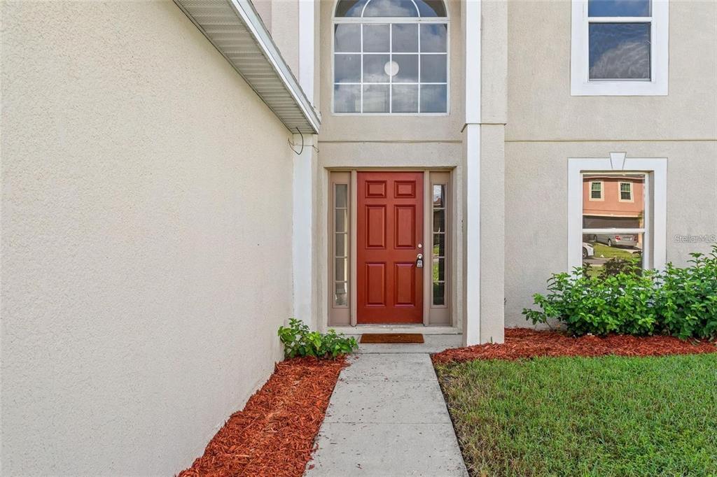 A red front door is centered on the exterior of a two-story stucco home — 14126 ECON WOODS LANE, ORLANDO, FL