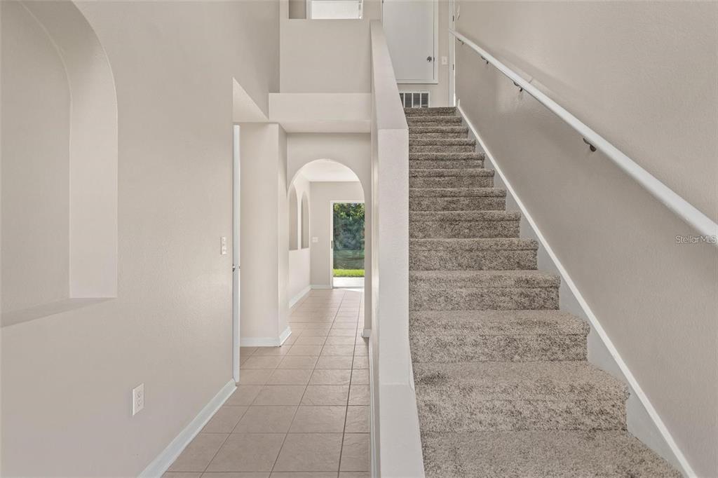 A carpeted staircase leads to an upper level next to a tiled hallway with arches — 14126 ECON WOODS LANE, ORLANDO, FL