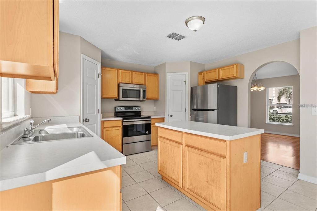 A kitchen features light wood cabinets, stainless steel appliances, a center island, and tile flooring — 14126 ECON WOODS LANE, ORLANDO, FL