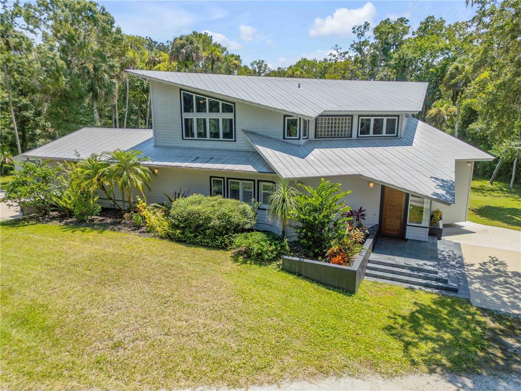 An exterior view of a modern house with a metal roof and lush landscaping — 2612 TURNBULL BAY ROAD, NEW SMYRNA BEACH, FL