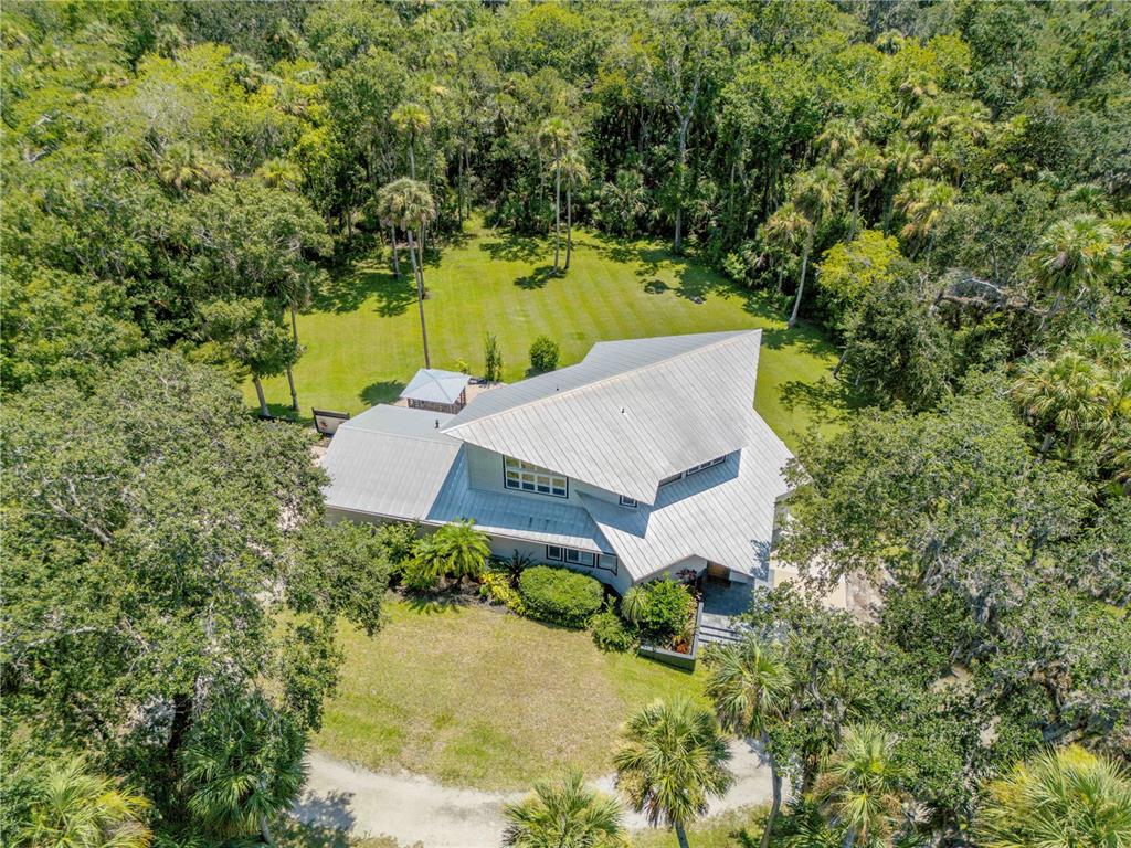 An aerial view shows a modern house with a metal roof surrounded by dense trees — 2612 TURNBULL BAY ROAD, NEW SMYRNA BEACH, FL