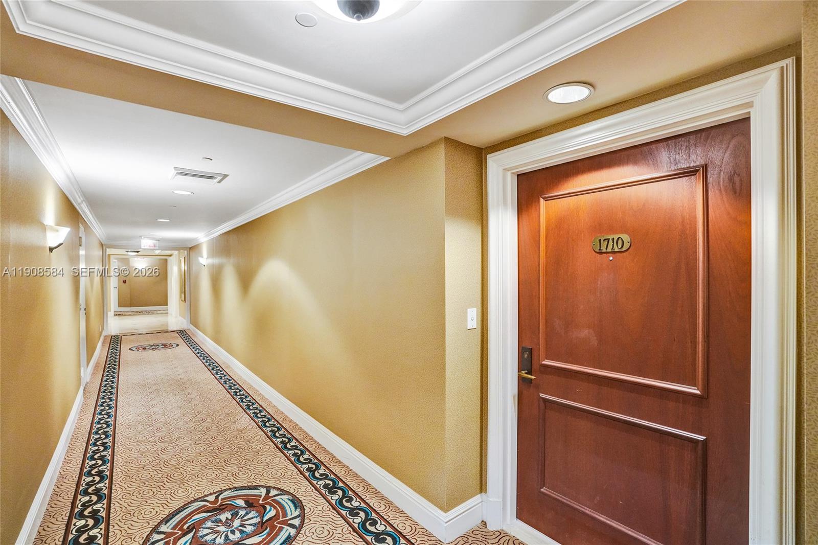 A hallway with tan walls, patterned carpet, and a wooden door labeled 1710 — 2000 Island Blvd # 1710, Aventura FL 33160, AVENTURA, FL