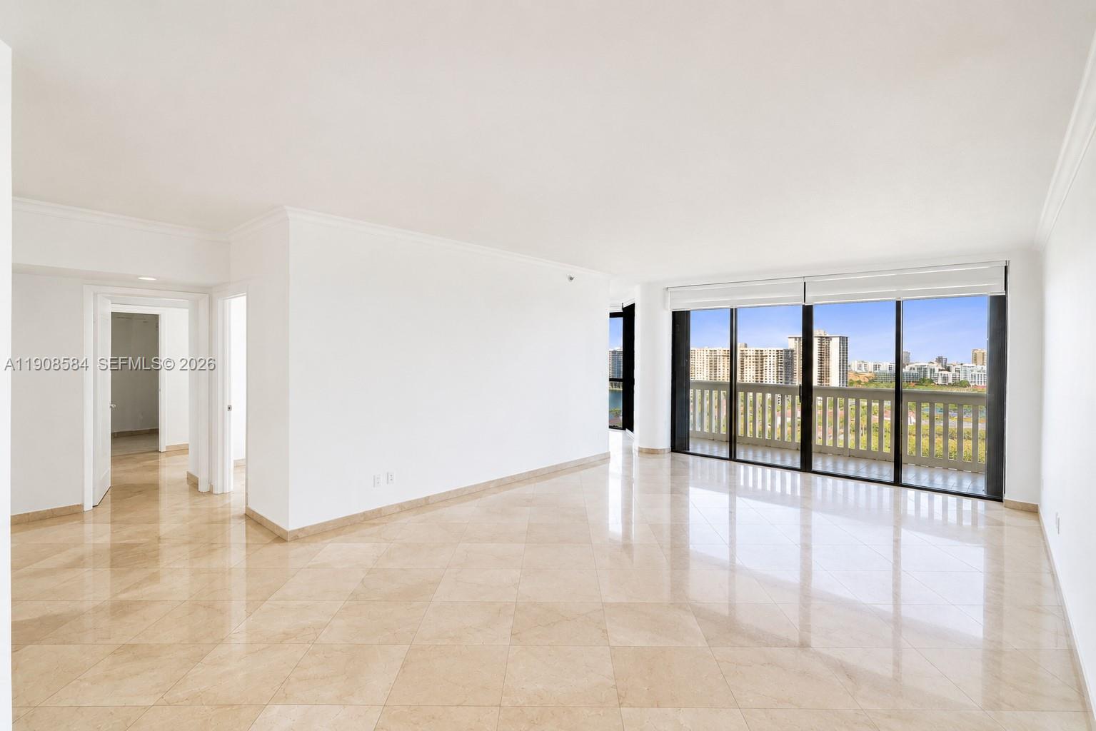 A bright, empty living room features beige tile floors, white walls, and large sliding glass doors — 2000 Island Blvd # 1710, Aventura FL 33160, AVENTURA, FL