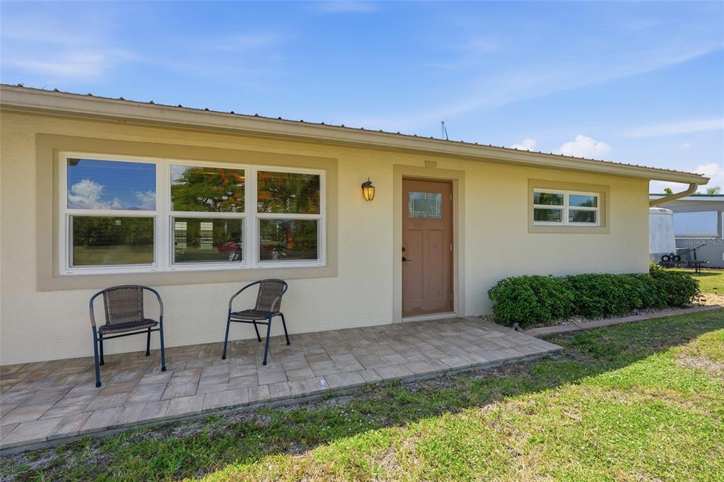 A single-story house exterior features a paved patio, two chairs, and a brown front door — 4310 PALM DRIVE, PUNTA GORDA, FL