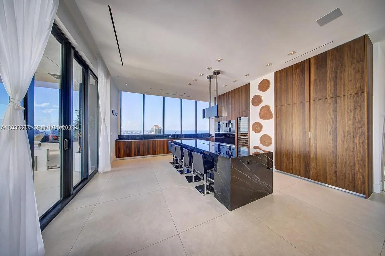 A modern kitchen features a black marble island, wood cabinetry, and floor-to-ceiling windows with ocean views — 17141 Collins Ave # 4602, Sunny Isles Beach FL 33160, SUNNY ISLES BEACH, FL