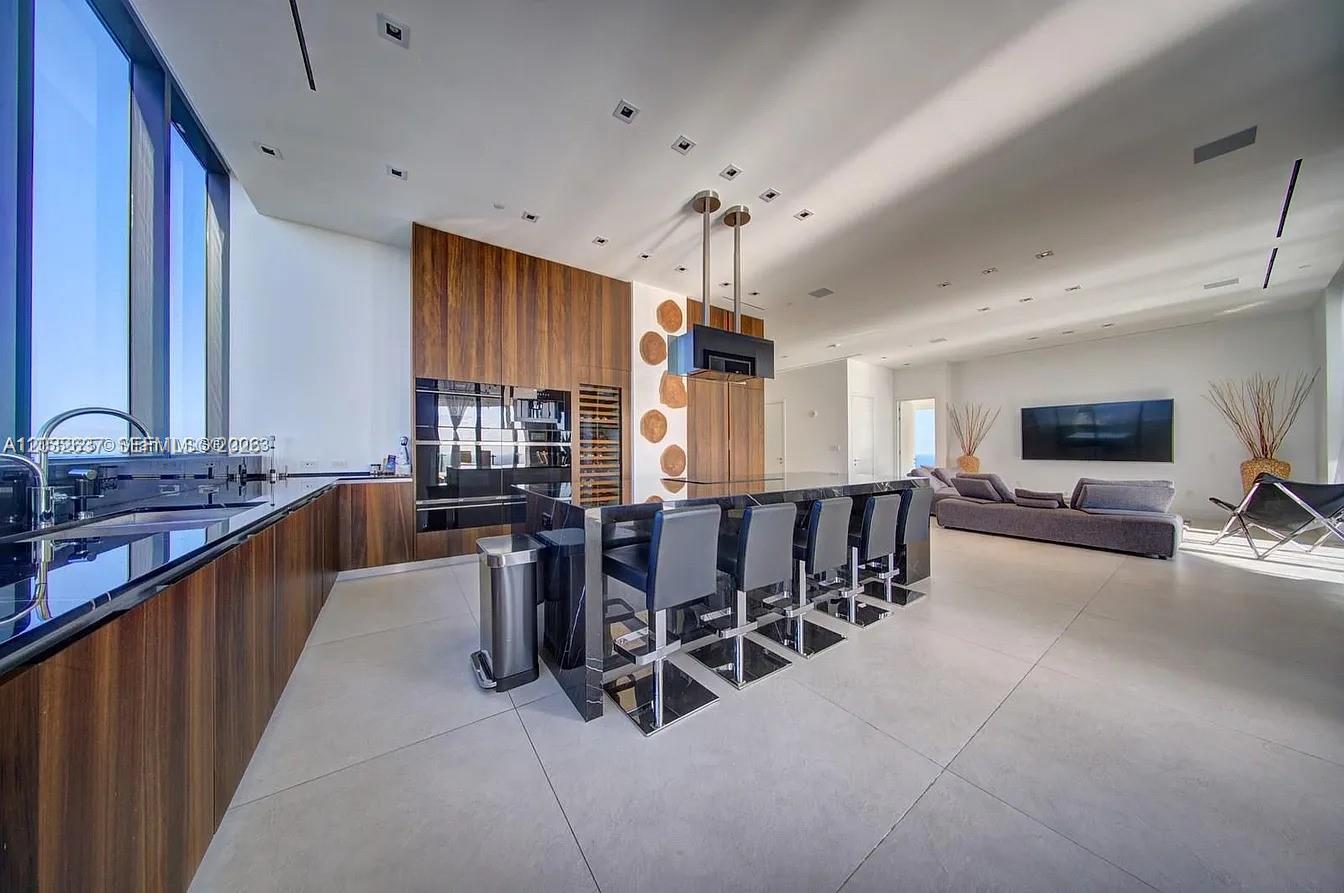A modern kitchen features dark wood cabinetry, a black island with bar stools, and tile flooring — 17141 Collins Ave # 4602, Sunny Isles Beach FL 33160, SUNNY ISLES BEACH, FL
