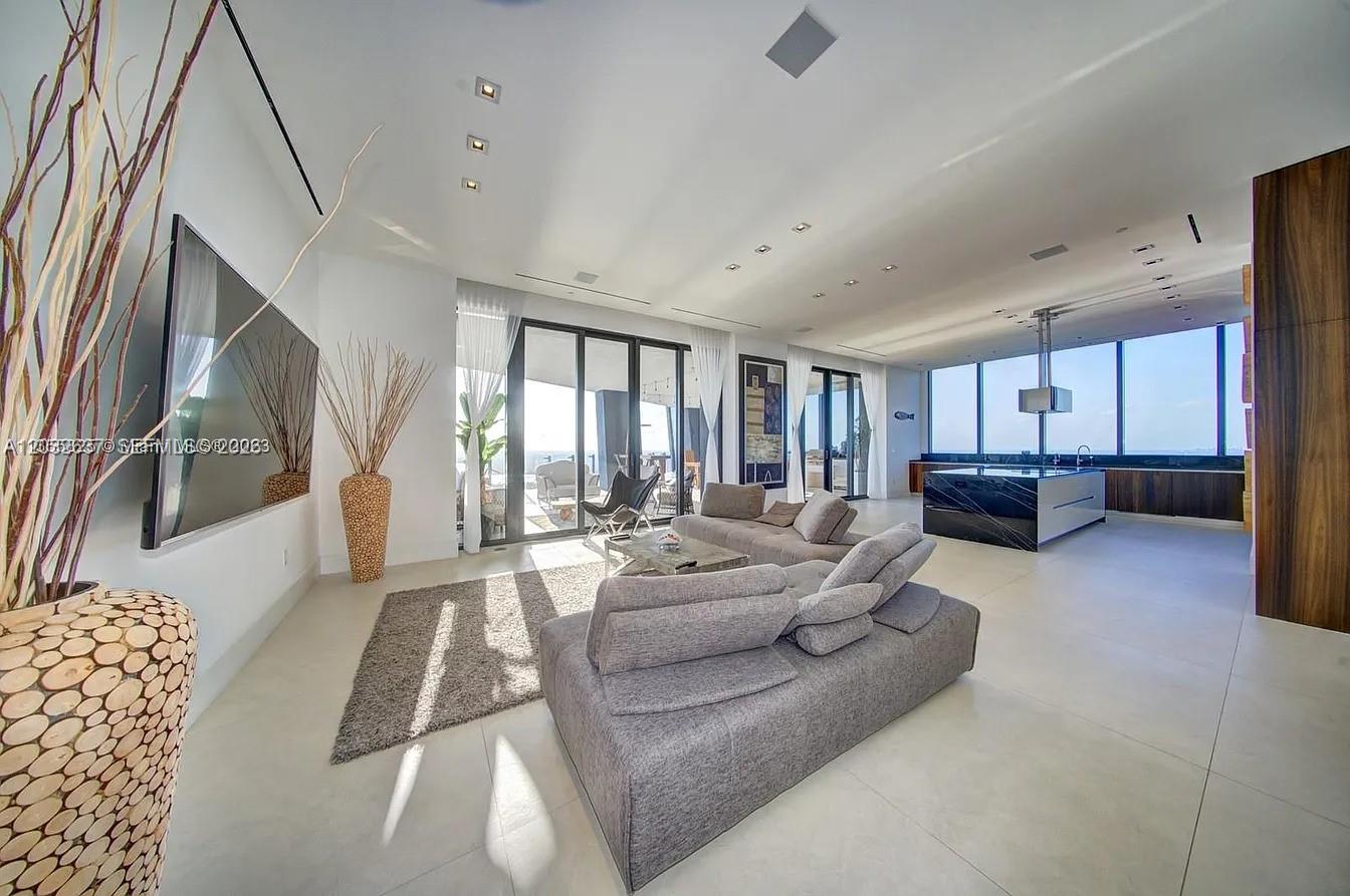 A modern open-concept living room features a gray sofa, kitchen island, and floor-to-ceiling windows — 17141 Collins Ave # 4602, Sunny Isles Beach FL 33160, SUNNY ISLES BEACH, FL