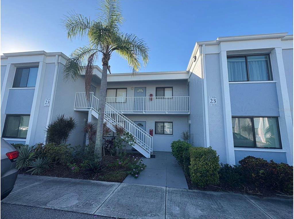 A two-story apartment building exterior features a central staircase, a palm tree, and balconies — 5310 26TH STREET W UNIT 2302, BRADENTON, FL