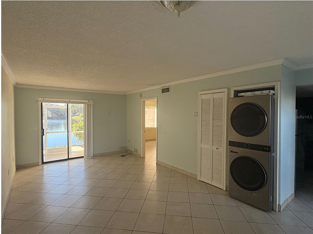 An open living area with tile flooring, a sliding glass door, and a stacked laundry unit — 5310 26TH STREET W UNIT 2302, BRADENTON, FL