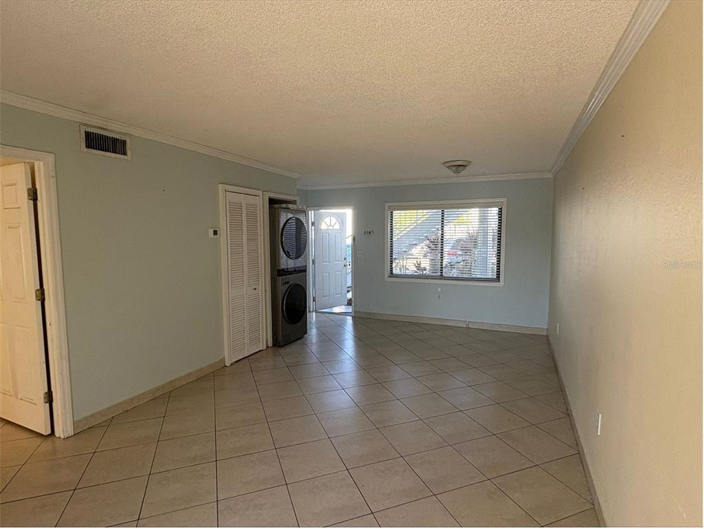 An interior view of a room with light-colored walls, tile flooring, and a stacked laundry unit — 5310 26TH STREET W UNIT 2302, BRADENTON, FL