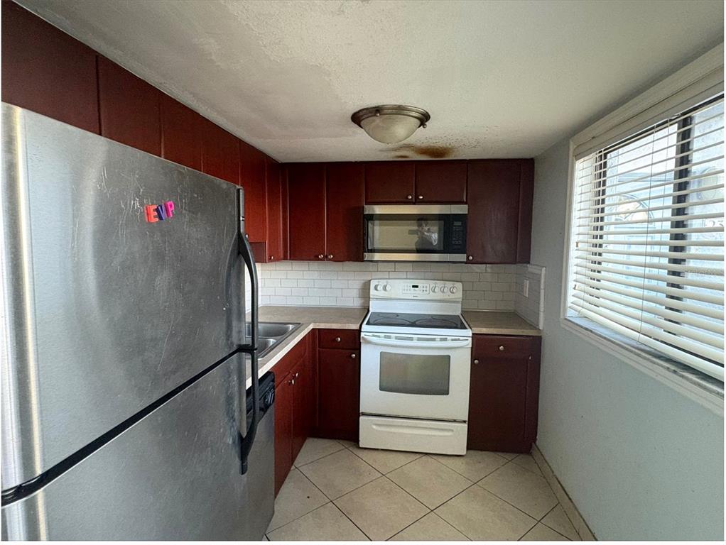 A kitchen features dark wood cabinets, stainless steel appliances, a white tile backsplash, and tile flooring — 5310 26TH STREET W UNIT 2302, BRADENTON, FL