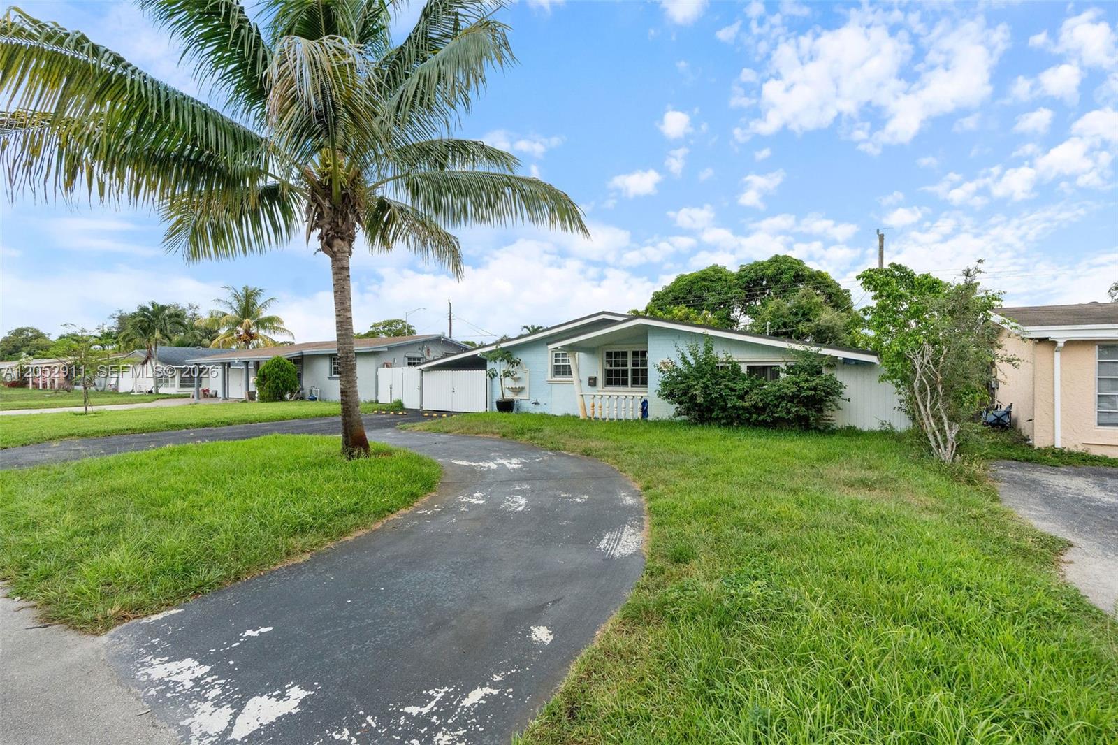 A light blue single-story house features a curved driveway and a prominent palm tree — 7501 Granada Blvd, Miramar FL 33023, MIRAMAR, FL