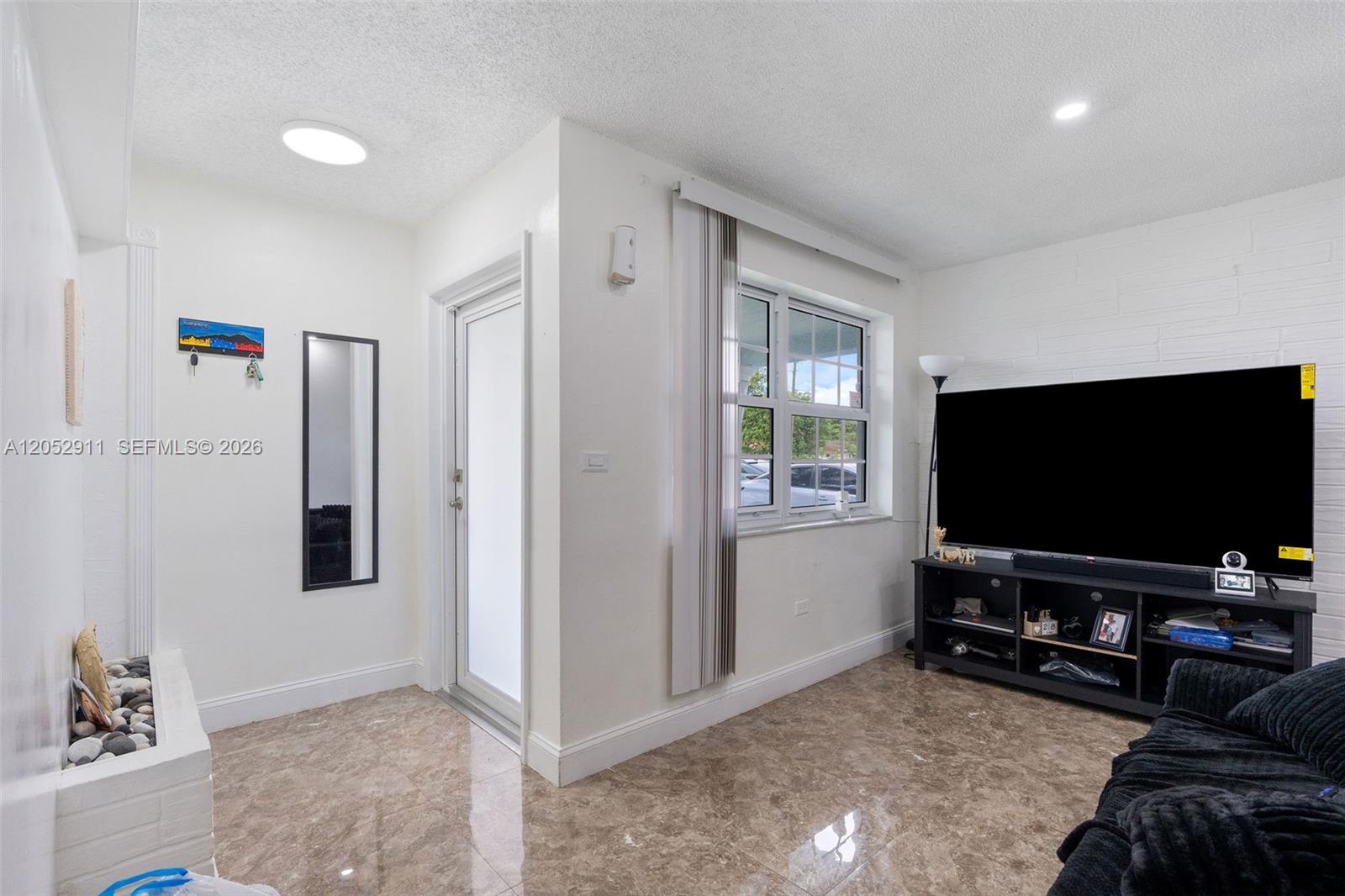 A living room features white walls, a large television, and light-colored marble-style tile flooring — 7501 Granada Blvd, Miramar FL 33023, MIRAMAR, FL
