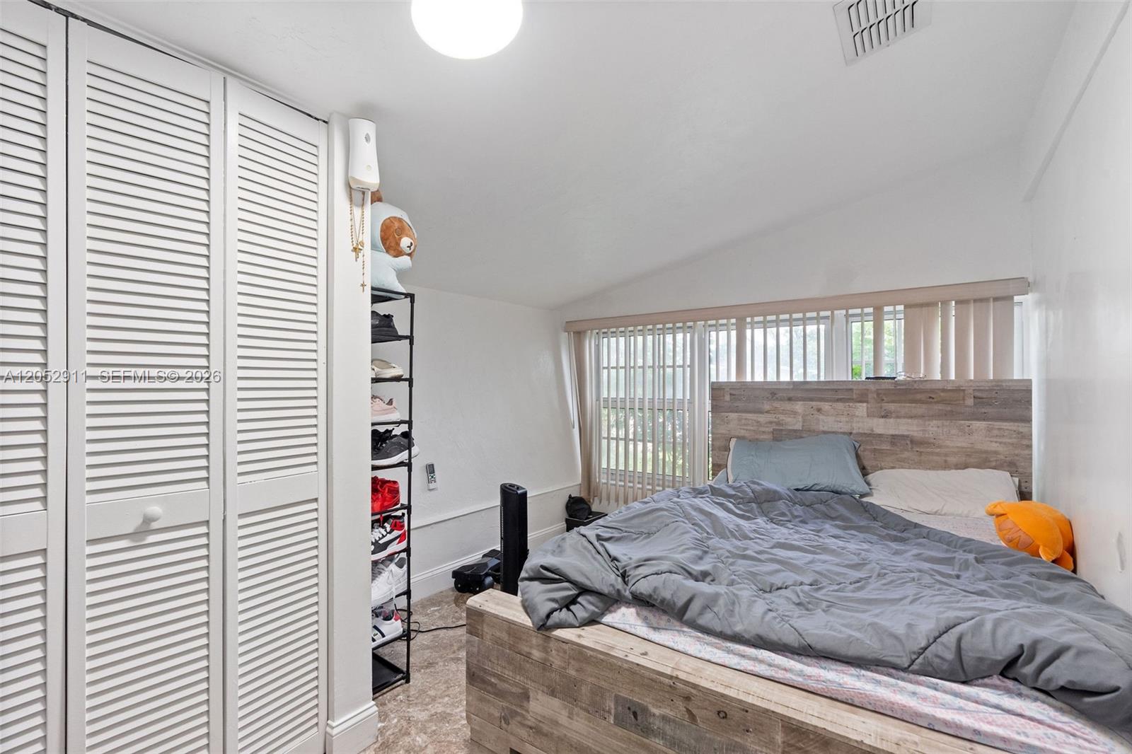 A bedroom features a wooden bed frame, a tall shoe rack, and white louvered closet doors — 7501 Granada Blvd, Miramar FL 33023, MIRAMAR, FL