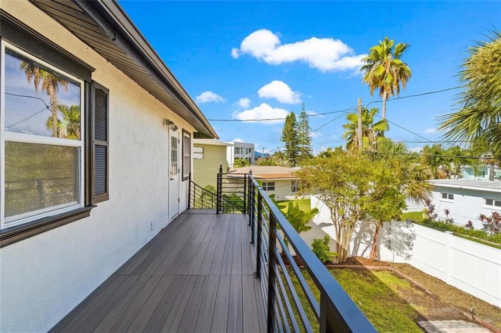 An elevated wooden deck with black metal railings overlooks a backyard with palm trees — 307 161ST AVENUE, REDINGTON BEACH, FL