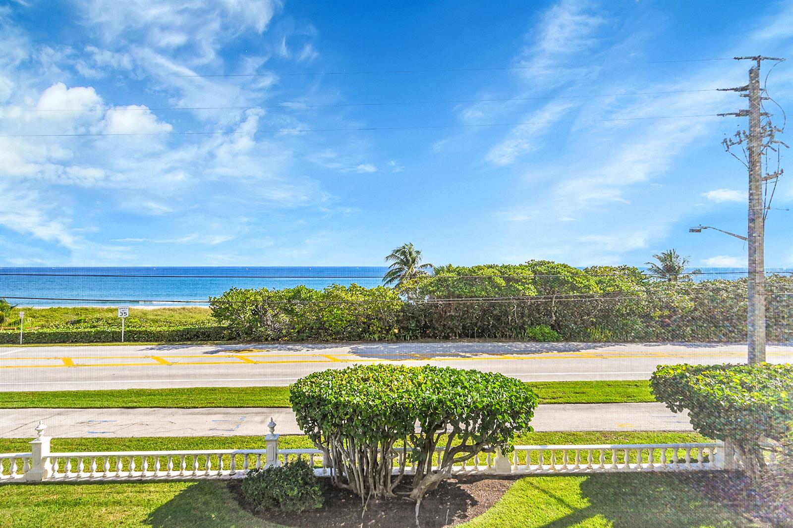 A view from a balcony overlooking a road, lush greenery, and the ocean — 2871 N Ocean Boulevard # D302, Boca Raton FL 33431, BOCA RATON, FL