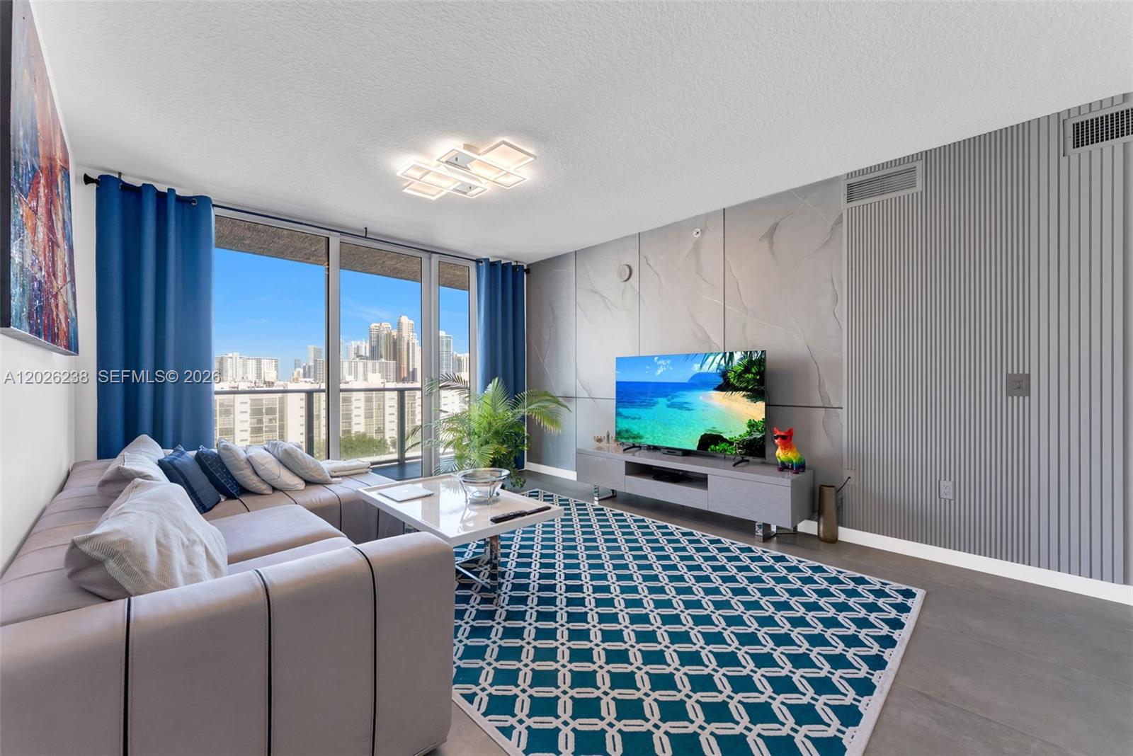A living room features a sectional sofa, a patterned rug, and a wall-mounted television — 300 Sunny Isles Blvd # 905, Sunny Isles Beach FL 33160, SUNNY ISLES BEACH, FL
