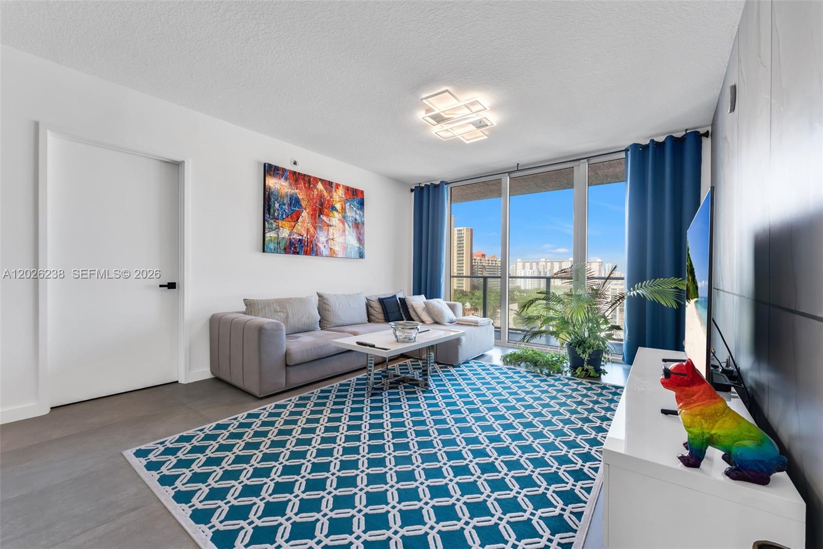 A living room features a grey sectional sofa, a geometric rug, and a balcony view — 300 Sunny Isles Blvd # 905, Sunny Isles Beach FL 33160, SUNNY ISLES BEACH, FL