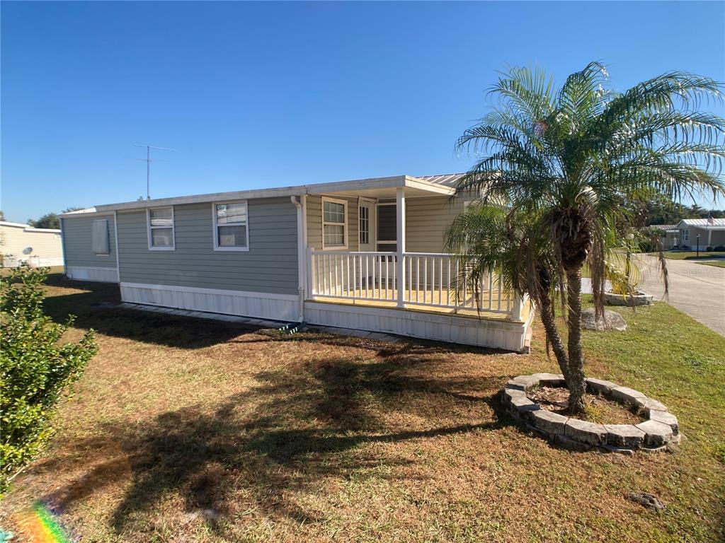 A light green mobile home features a wooden front porch and a palm tree — 1710 7TH STREET SW UNIT 44, RUSKIN, FL